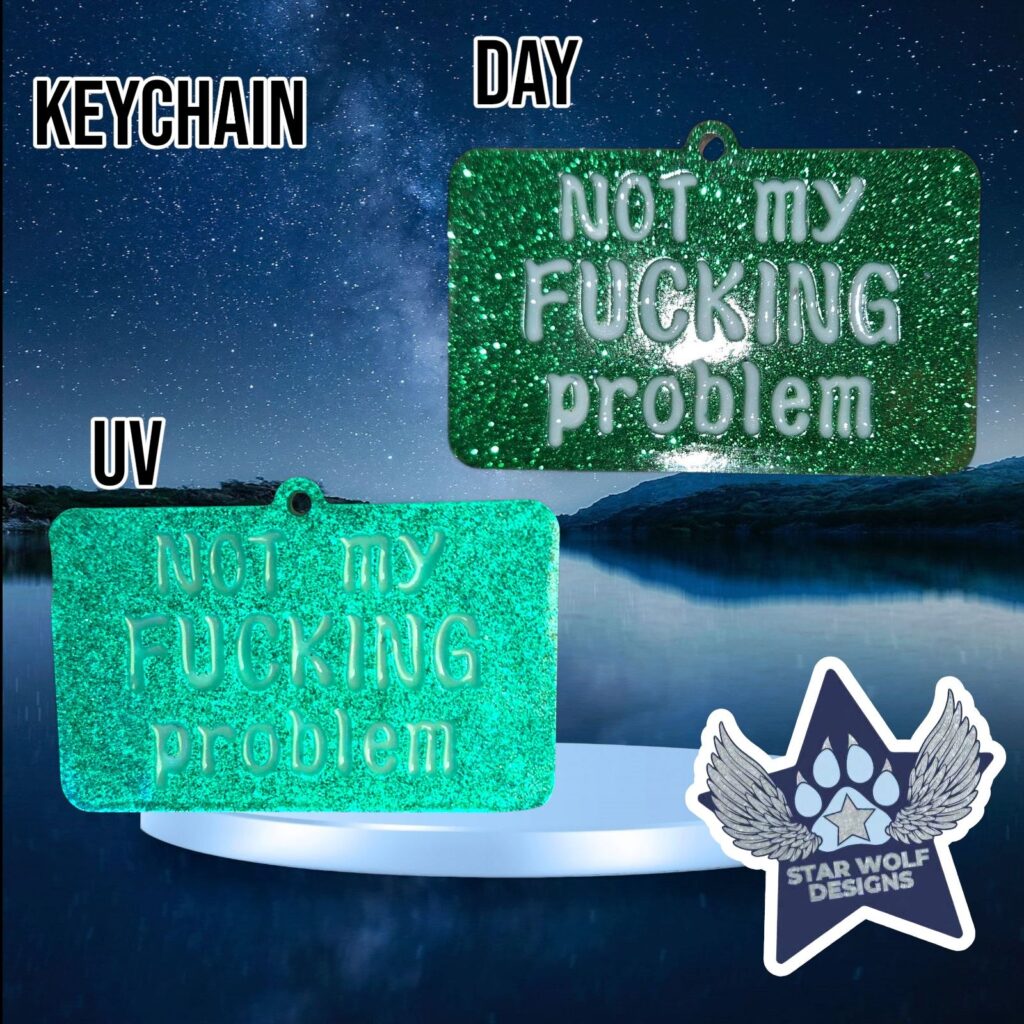 Green glitter keychain reading “Not my fucking problem,” shown in daylight and under UV light